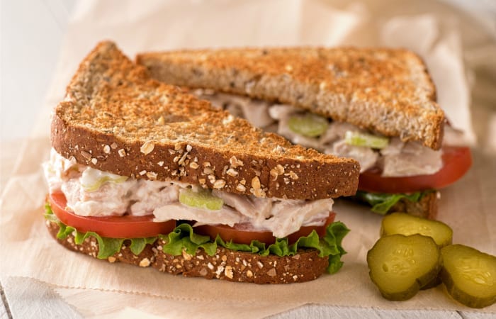 toasted tuna salad sandwich with tomatoes, lettuce, and pickles on wheat bread