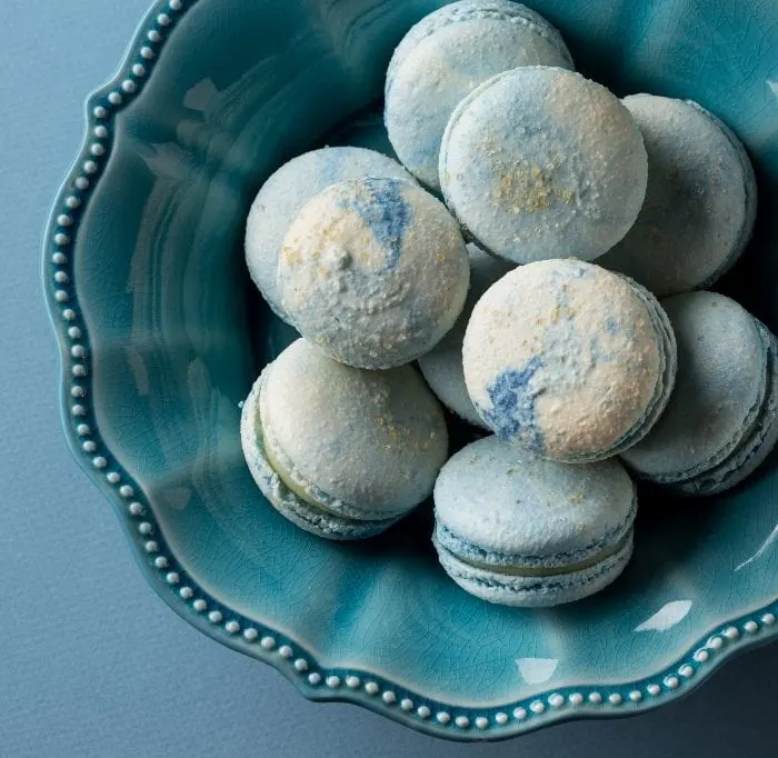 Blue Cotton Candy flavored French macaron cookies in a blue bowl on blue background.