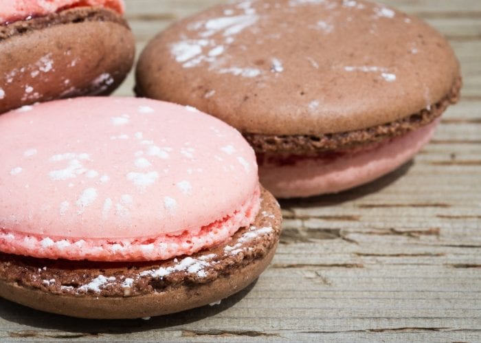 Strawberry and chocolate flavored macaron cookies on a wood background.